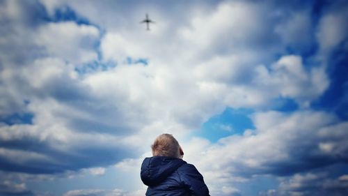 Low angle view of boy standing against cloudy sky