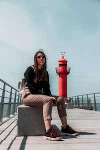 Portrait of young woman sitting on railing against sky