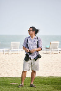 Full length of man with cameras standing on land against sea