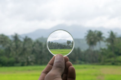 Close-up of hand holding glass on field against sky