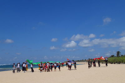 People with flag at beach against blue sky