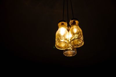 Close-up of illuminated light bulb hanging against black background