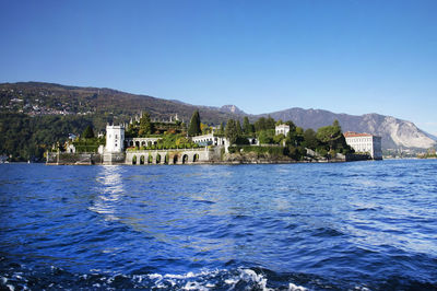 Buildings by sea against clear blue sky