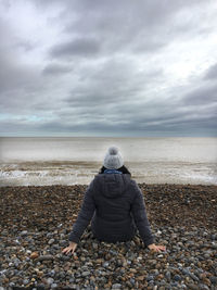 Rear view of woman sitting on pebble beach looking out to sea