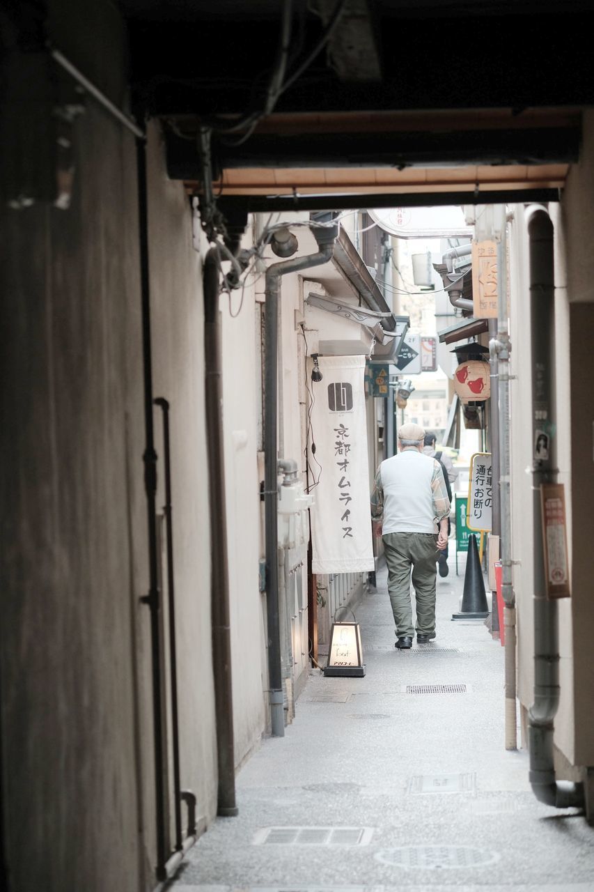 REAR VIEW OF MAN WALKING IN CORRIDOR OF BUILDING