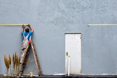 A workman applies tape at the height to which he has to paint the house wall