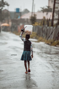 Rear view of girl carrying bucket on road during rain