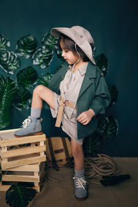 Serious boy child traveler in a hat stand on wooden boxes in a studio on a green background