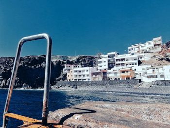 Buildings by sea against clear blue sky