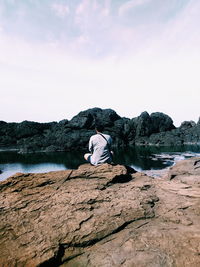 Rear view of man sitting on rock against sky