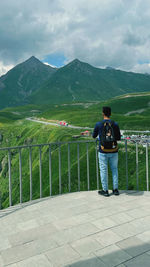 Rear view of man standing on railing against mountains