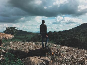 Rear view of man standing on mountain against cloudy sky