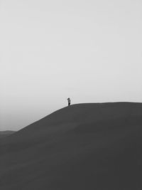 Distant person standing on sand dune against clear sky