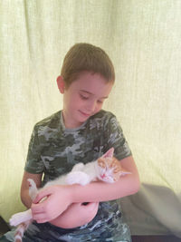Boy holding kitten  standing against wall