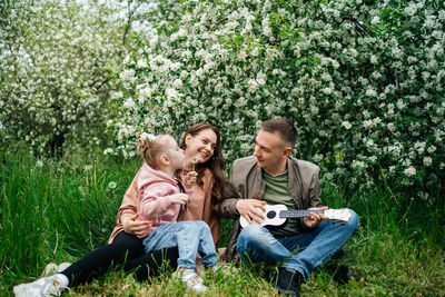 Family mom mom baby daughter in the garden blooming apple trees, father playing the ukulele