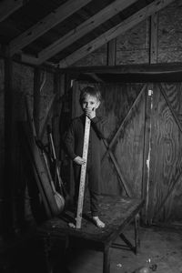 Portrait of boy with yardstick on table in wooden garage