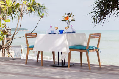 Chairs and table on beach by sea against sky