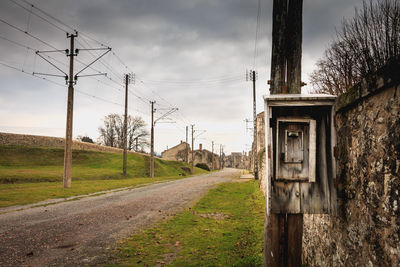 Road by electricity pylon against sky