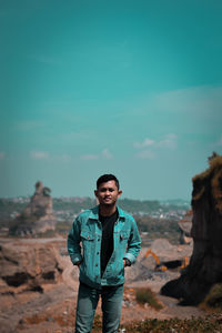 Portrait of man standing on rock against blue sky