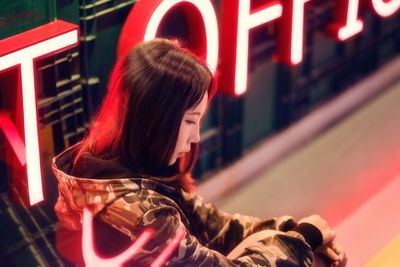 Side view of thoughtful woman sitting by neon sign at night