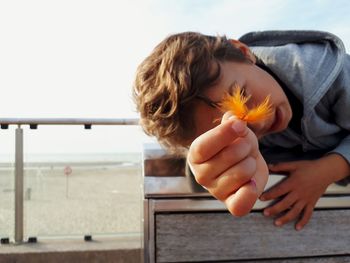 Midsection of woman holding orange while sitting on railing against sky