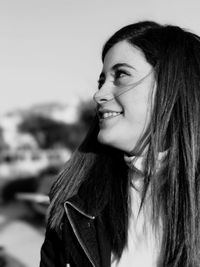 Smiling young woman looking away while standing against sky