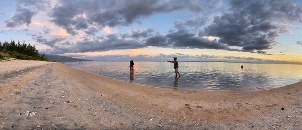 People on beach against sky during sunset