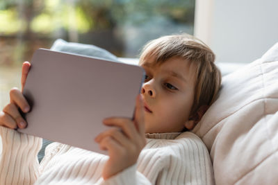 Boy spends time behind a screen on tablet on sofa in the living room. digital device. technologies.