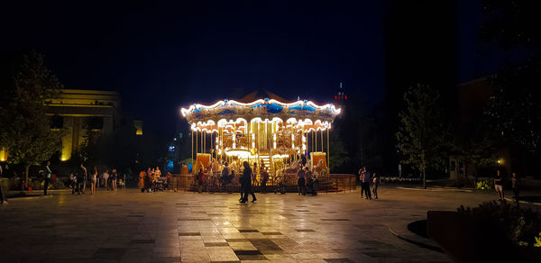 Illuminated amusement park against clear sky at night