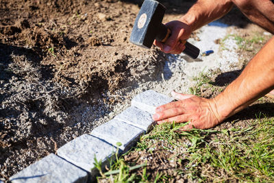 Cropped image of man hammering cobblestone on field