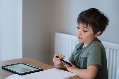 Boy looking away while sitting on table at home