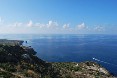 Scenic view of sea by mountain against cloudy sky