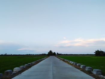 Empty footpath in field against sky