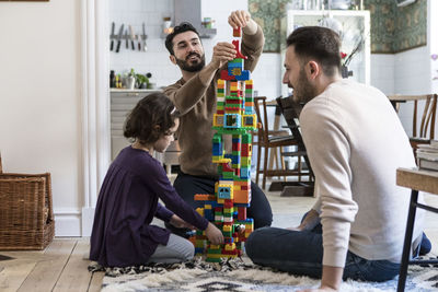 Happy gay men playing blocks with daughter at home