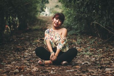 Smiling young woman sitting on land in forest