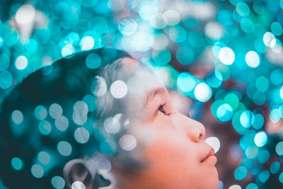 Close-up of boy looking up amidst illuminated lights