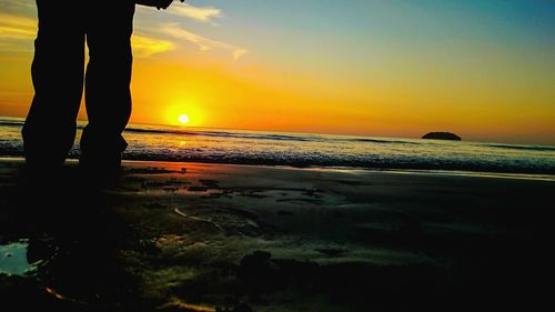 Low section of silhouette man on beach against sunset sky