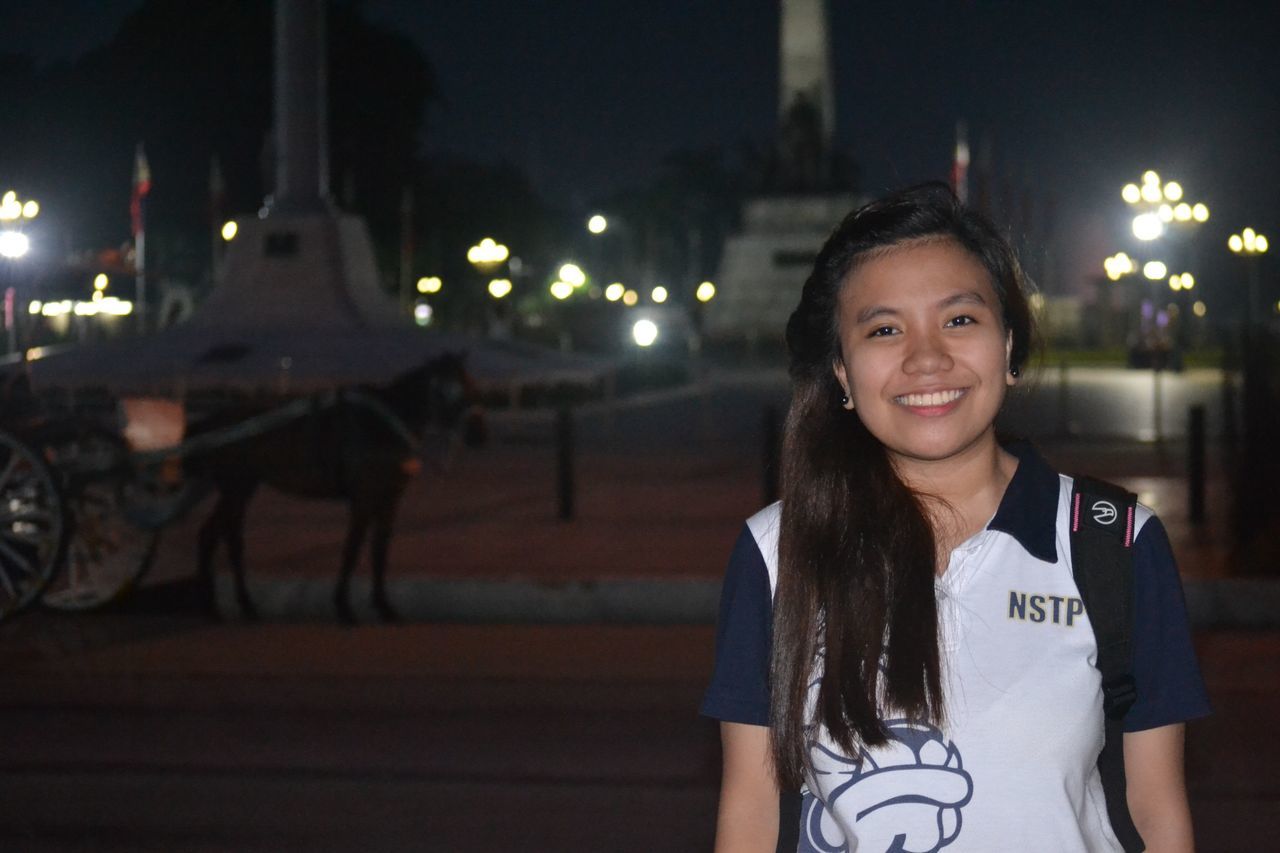 night, illuminated, lifestyles, leisure activity, looking at camera, young adult, portrait, casual clothing, front view, standing, waist up, incidental people, person, street, celebration, happiness, focus on foreground, smiling