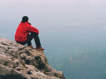 Hiker man take a rest on mountain peak. man sit on sharp summit and enjoy spectacular view.