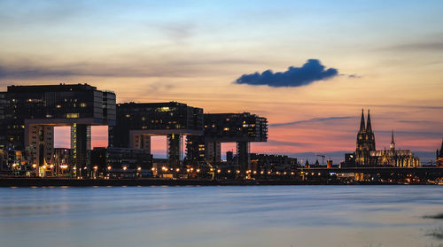 Illuminated buildings by sea against sky at sunset