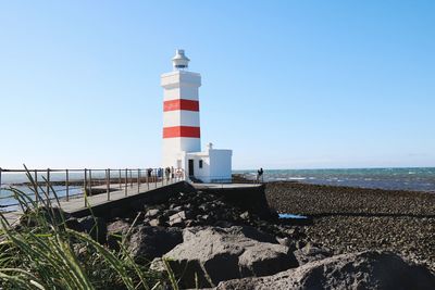 Lighthouse by sea against clear sky