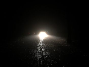 Illuminated lighting equipment on snow against sky at night