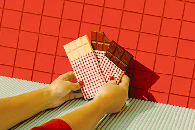 Woman hands holding chocolate bars against red tile wall