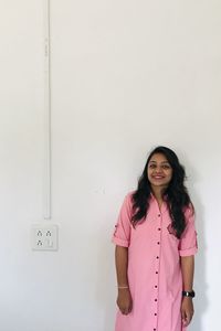 Portrait of smiling young woman standing against white wall