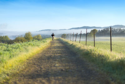 Man cycling on dirt road passing through landscape