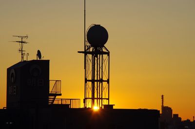 Silhouette water tower on building terrace during sunset