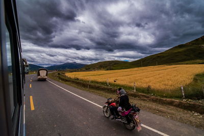 People riding motorcycle on road against cloudy sky
