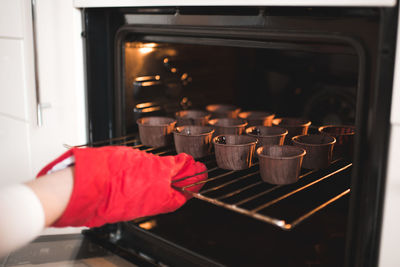 Woman put batter for chocolate cupcakes in oven in kitchen closeup. cooking time.