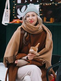 Young woman with blonde hair wearing brown fur coat eating sweet food on the christmas market. 
