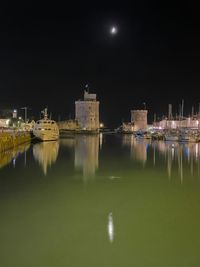 Illuminated city by sea against sky at night